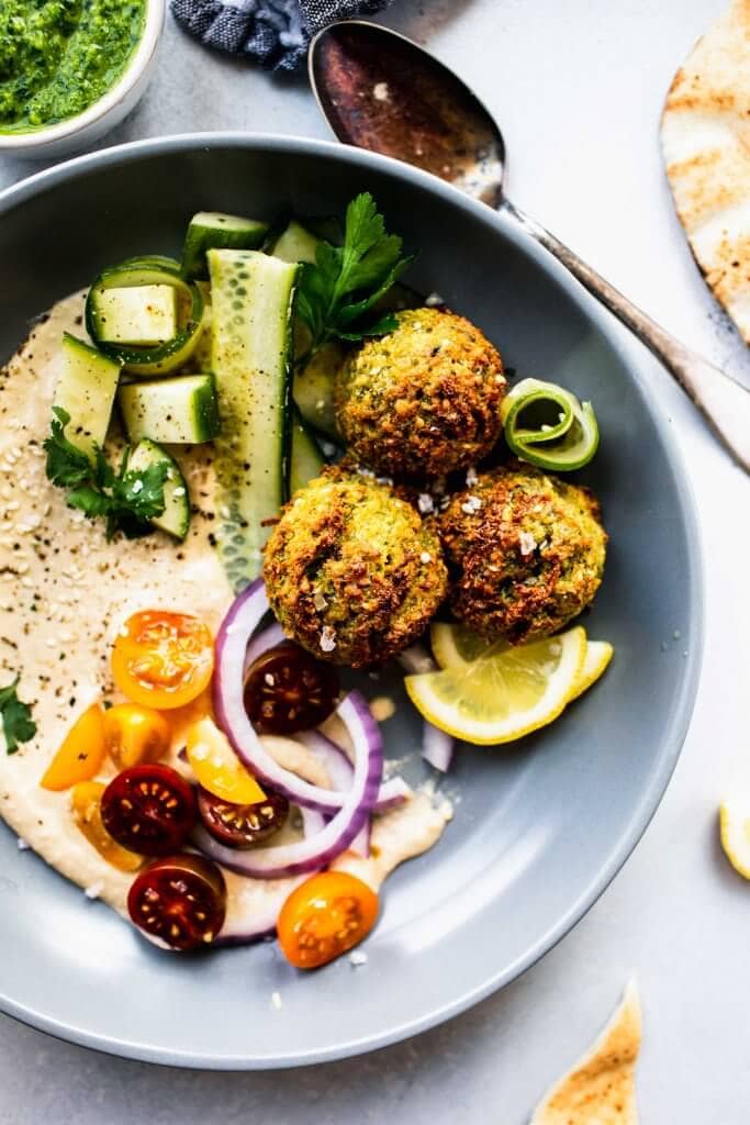 Three air fryer falafel balls in grey bowl with hummus, cucumber and cherry tomatoes.