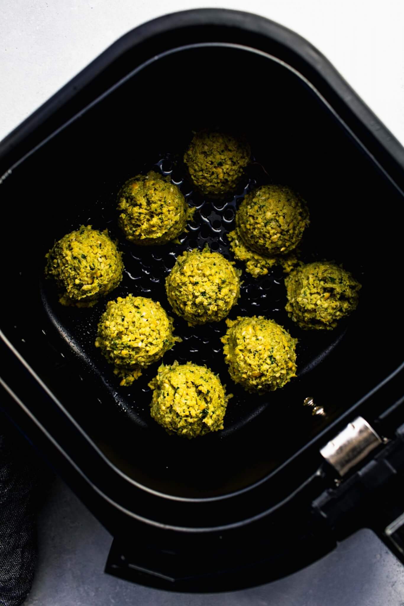 Uncooked falafel balls in air fryer basket.