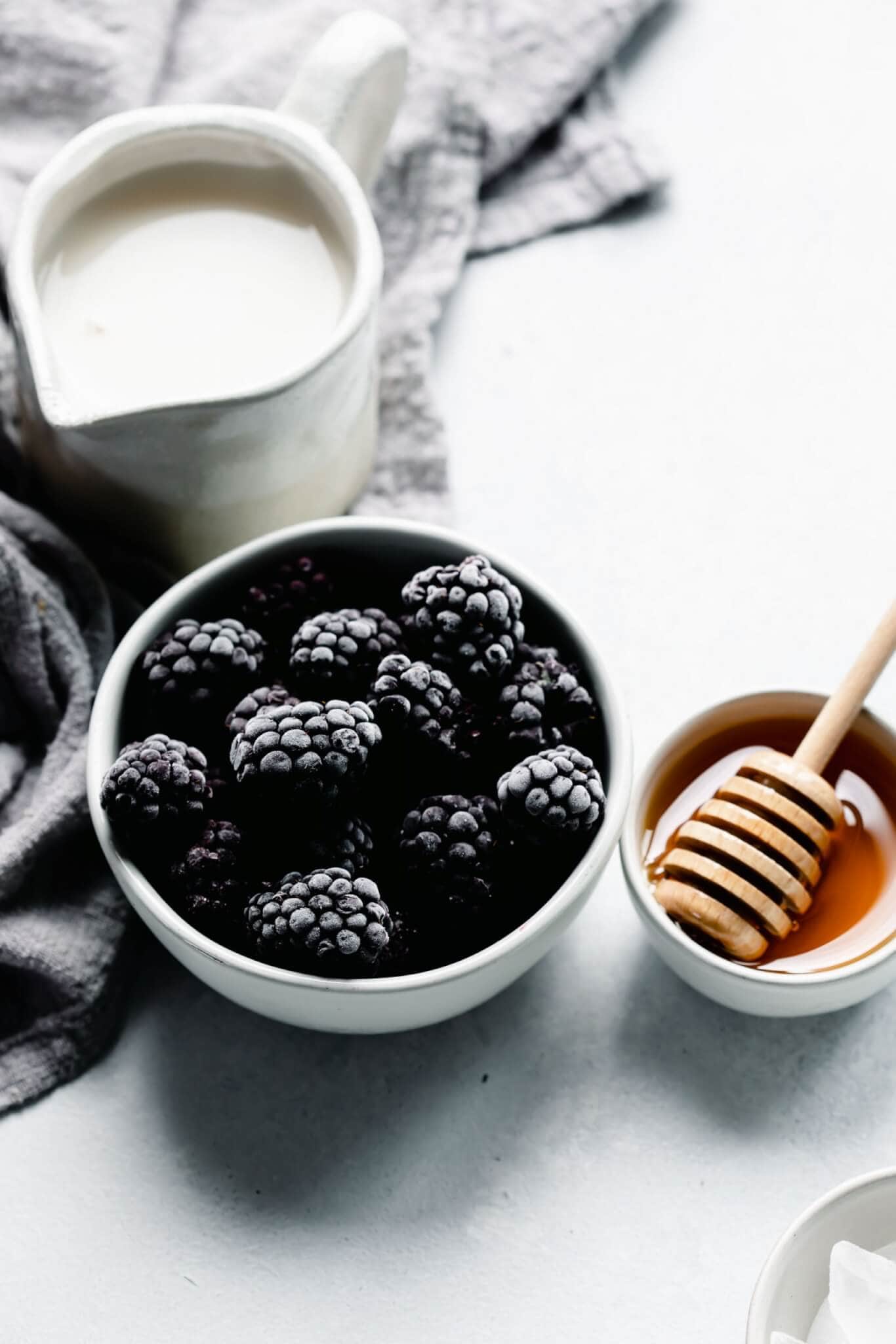 Bowl of frozen blackberries next to honey wand.