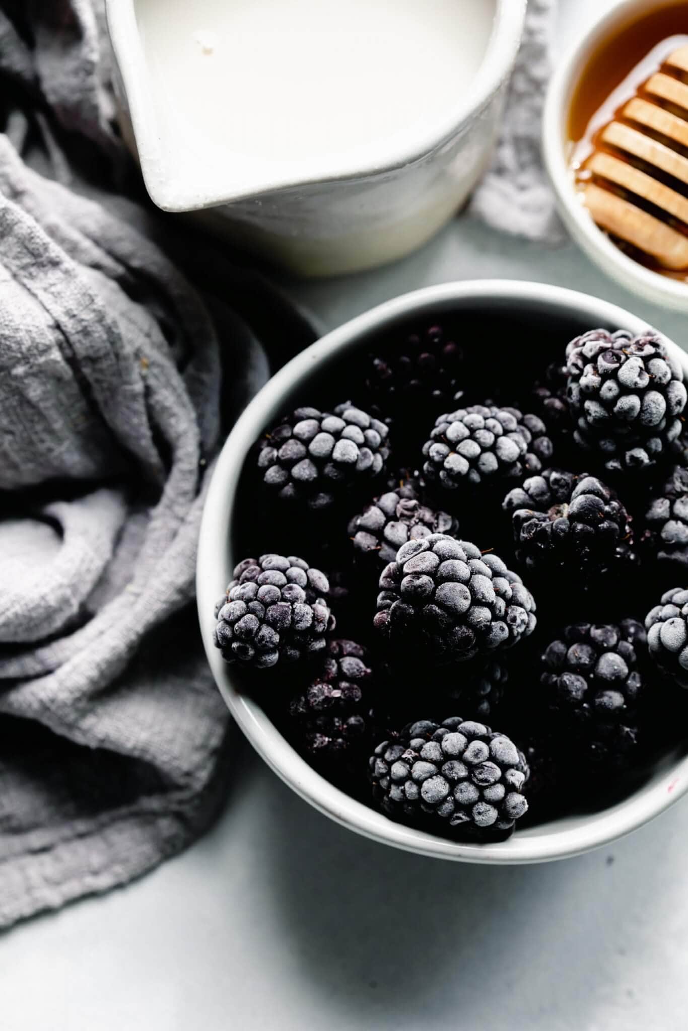 Bowl of frozen blackberries next to honey wand.