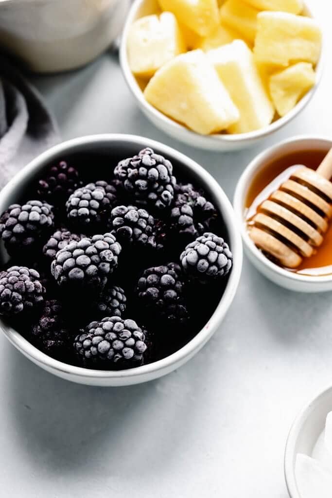 Bowl of frozen blackberries next to honey wand and bowl of frozen pineapple.