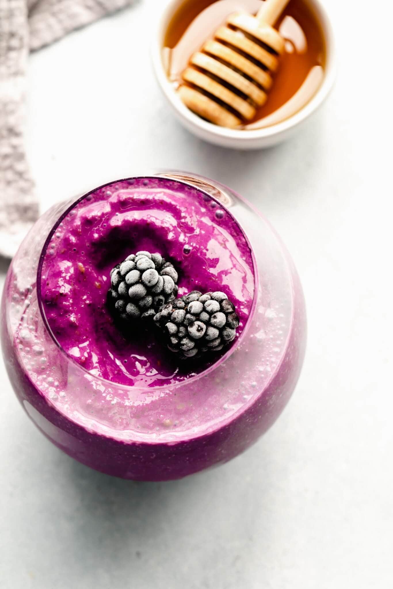 Overhead shot of blackberry smoothie in glass topped with frozen blackberries.