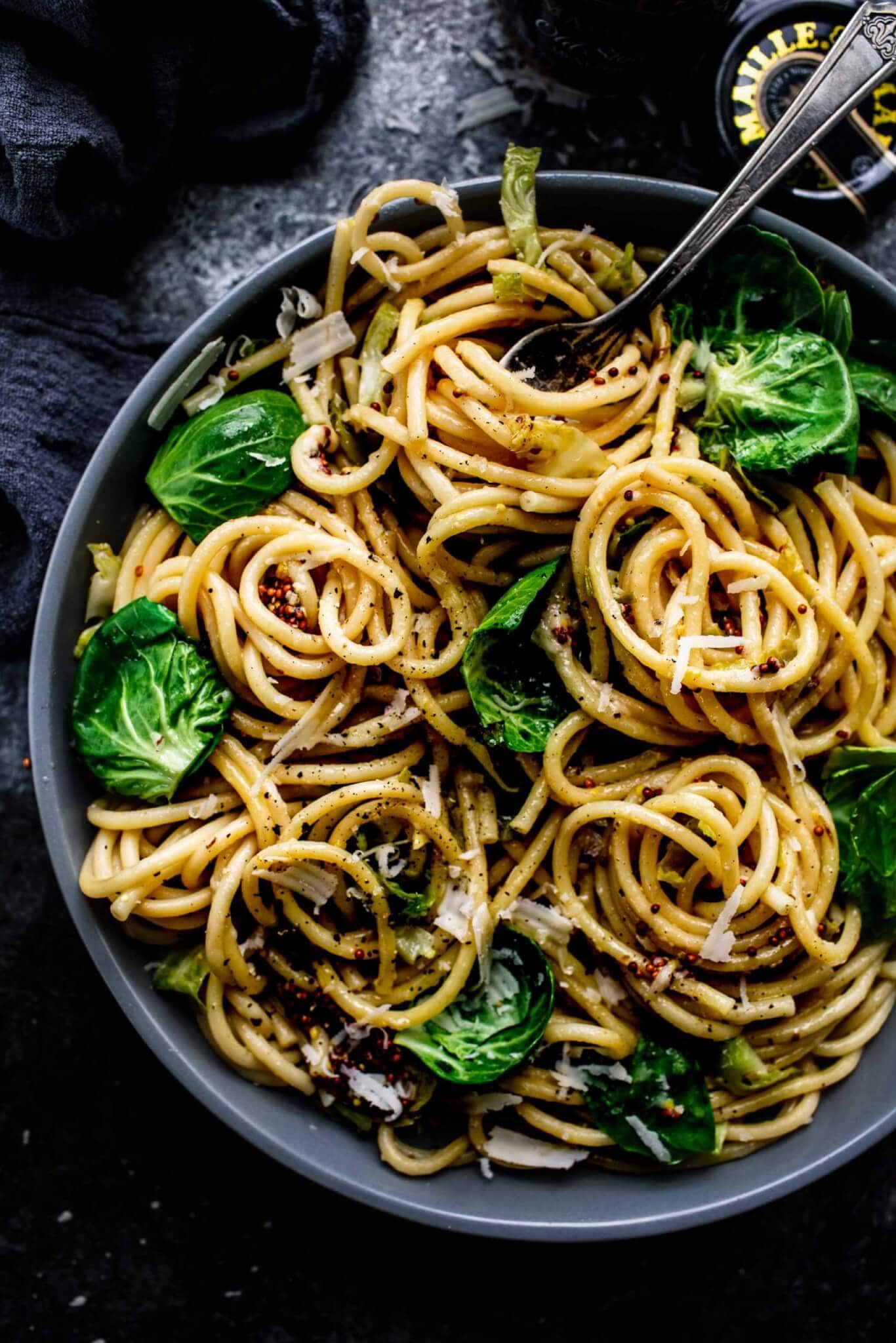 Brussels sprout pasta in grey bowl with fork twirling spaghetti.