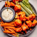 Buffalo cauliflower bites on plate with celery and carrot sticks and blue cheese dressing.
