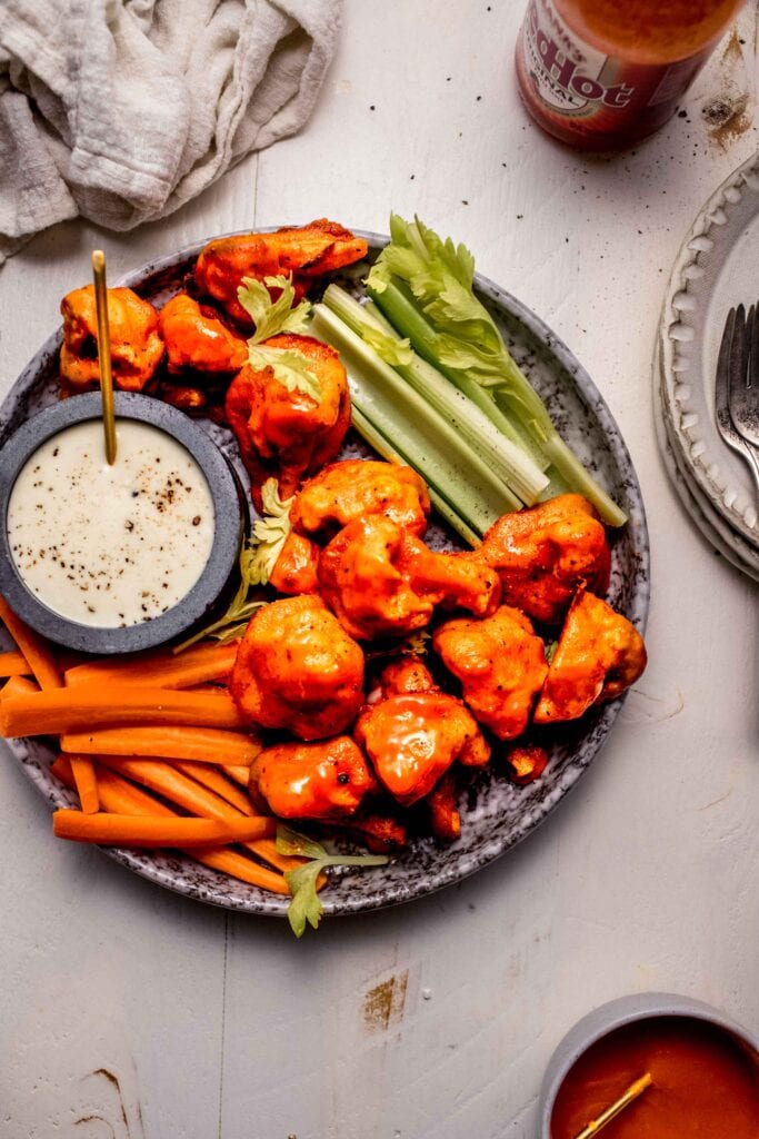 Buffalo cauliflower bites on plate with celery and carrot sticks and blue cheese dressing.