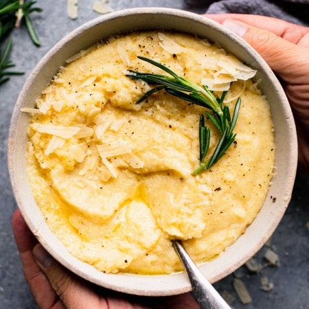 Two hands holding bowl of cooked polenta.
