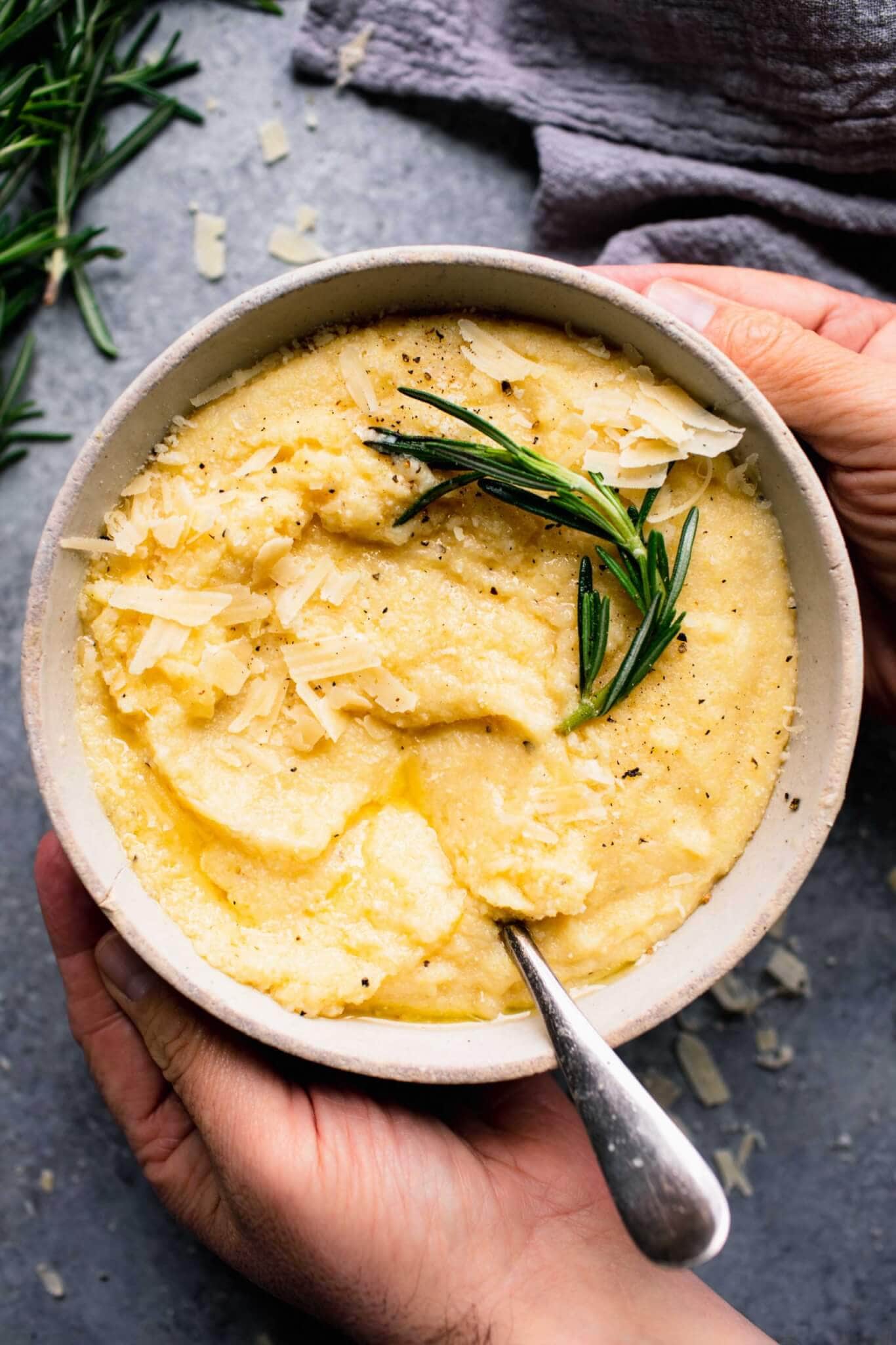 Two hands holding bowl of cooked polenta.