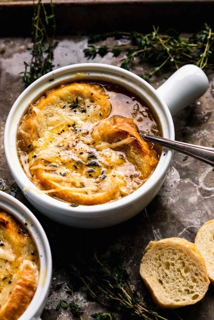 Side view of two bowls of french onion soup in crockery topped with baguette slices & melted cheese.