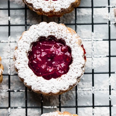 Overhead close up of linzer cookie dusted with powdered sugar and filled with strawberry jam.