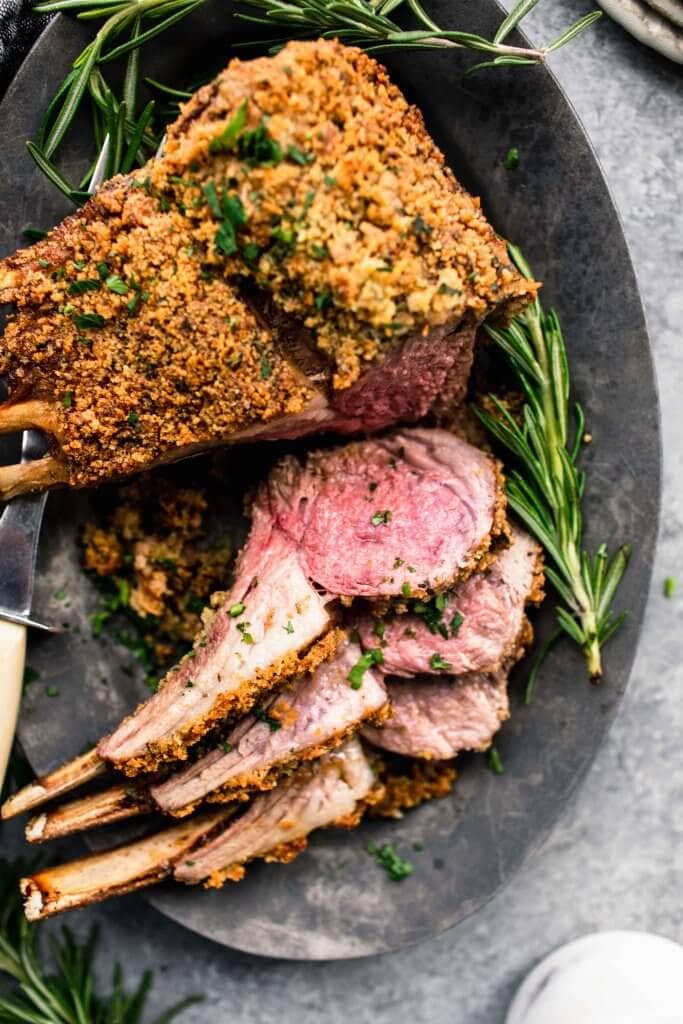 Herb crusted rack of lamb on grey serving platter with three chops sliced off.