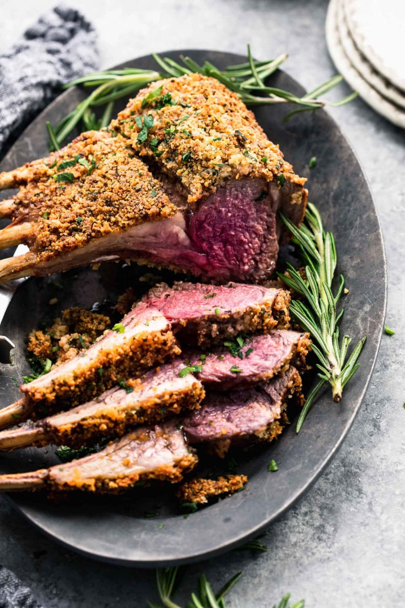 Herb crusted rack of lamb on grey serving platter with three chops sliced off.