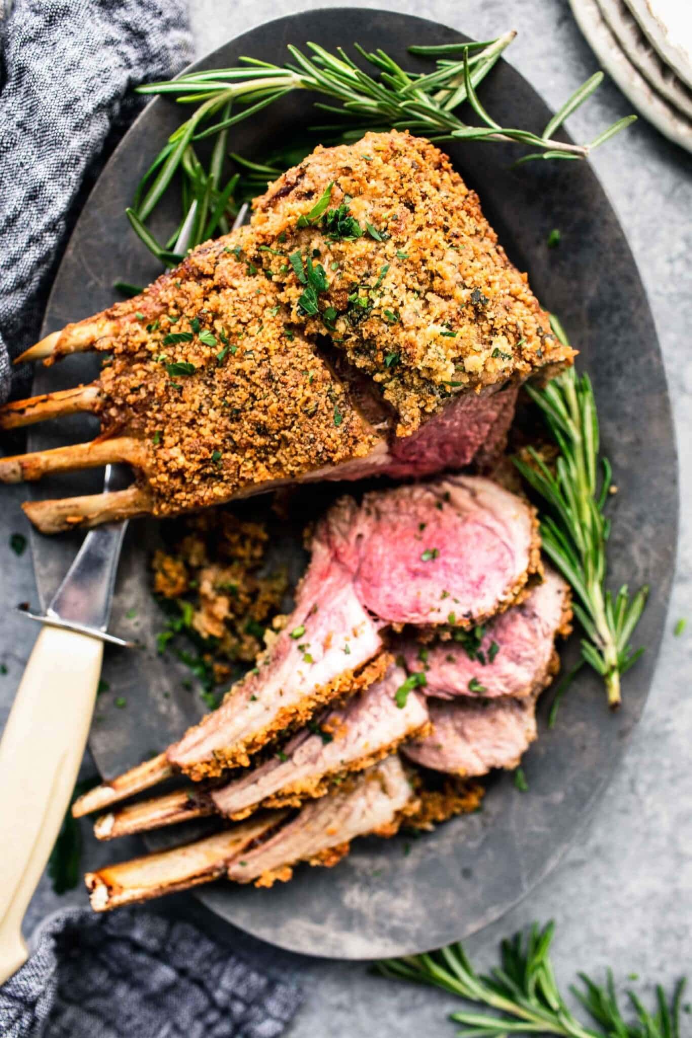 Herb crusted rack of lamb on grey serving platter with three chops sliced off.