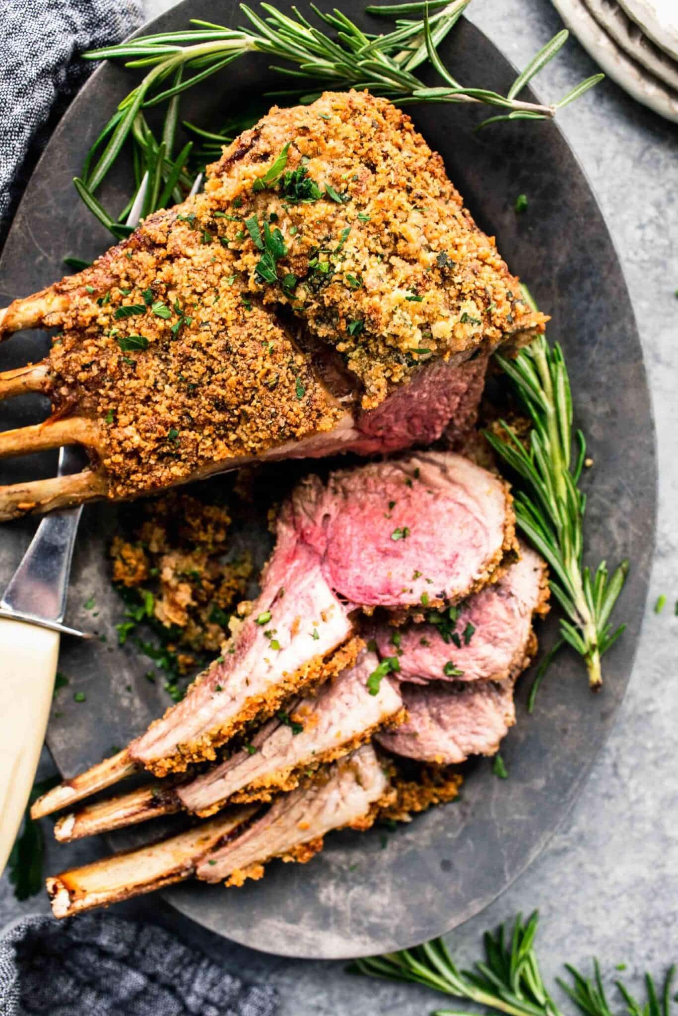 Herb crusted rack of lamb on grey serving platter with three chops sliced off.