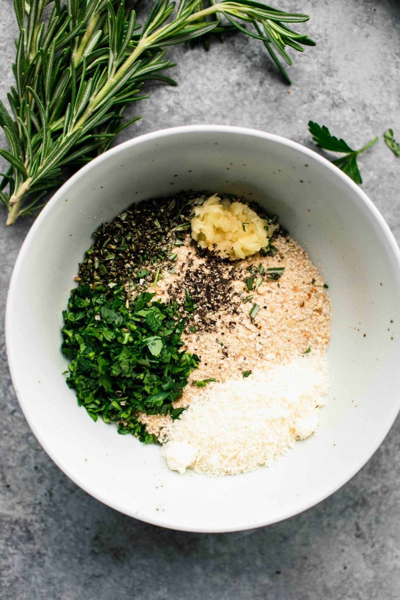 Breadcrumbs, herbs and parmesan cheese in small white bowl.