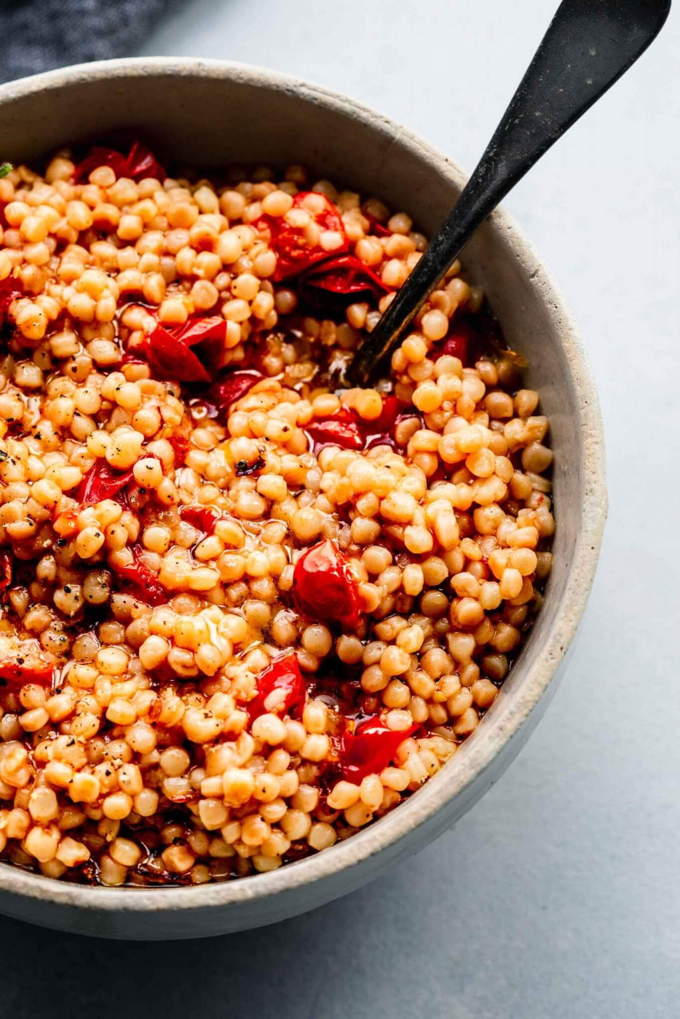 Side view of bowl of cooked tomato couscous with spoon.