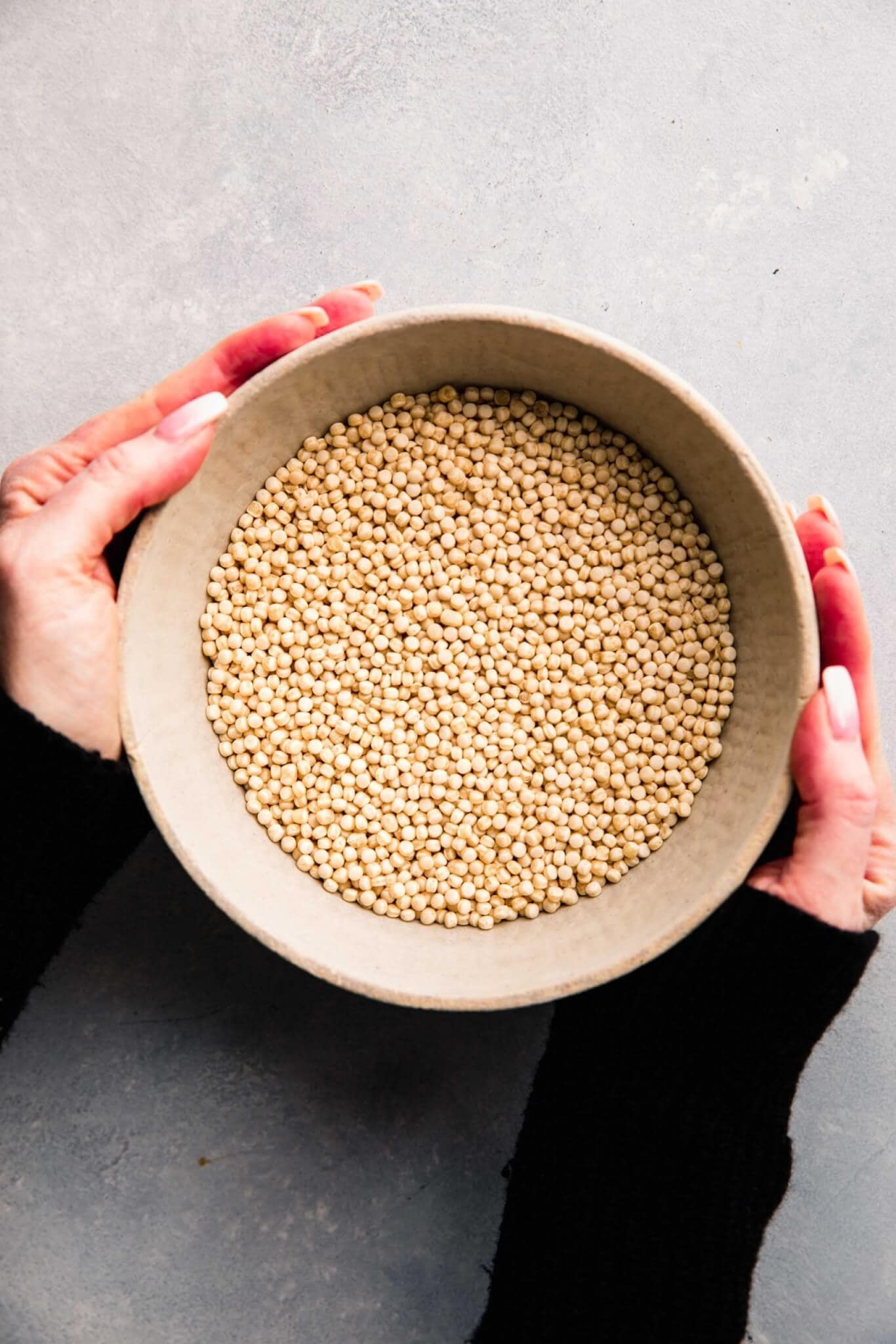 Two hands holding bowl of israeli couscous.