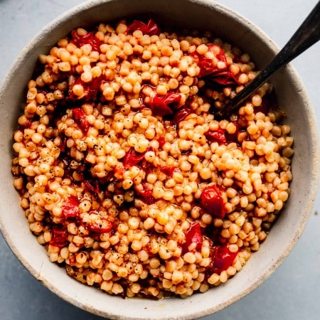 Overhead shot of bowl of cooked tomato couscous with spoon.