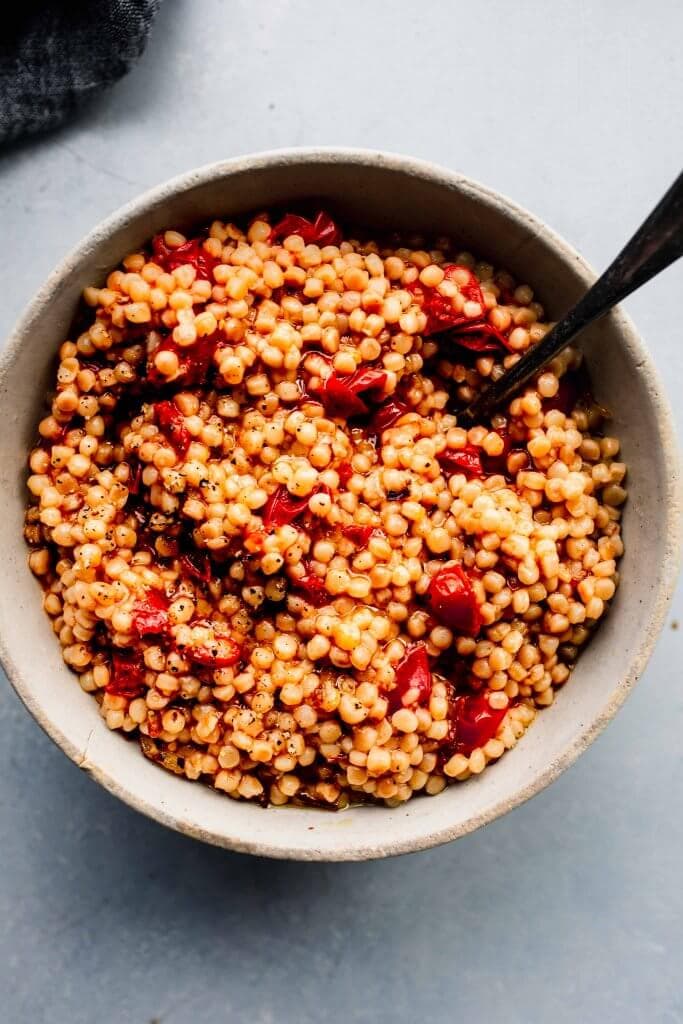 Overhead shot of bowl of cooked tomato couscous with spoon.