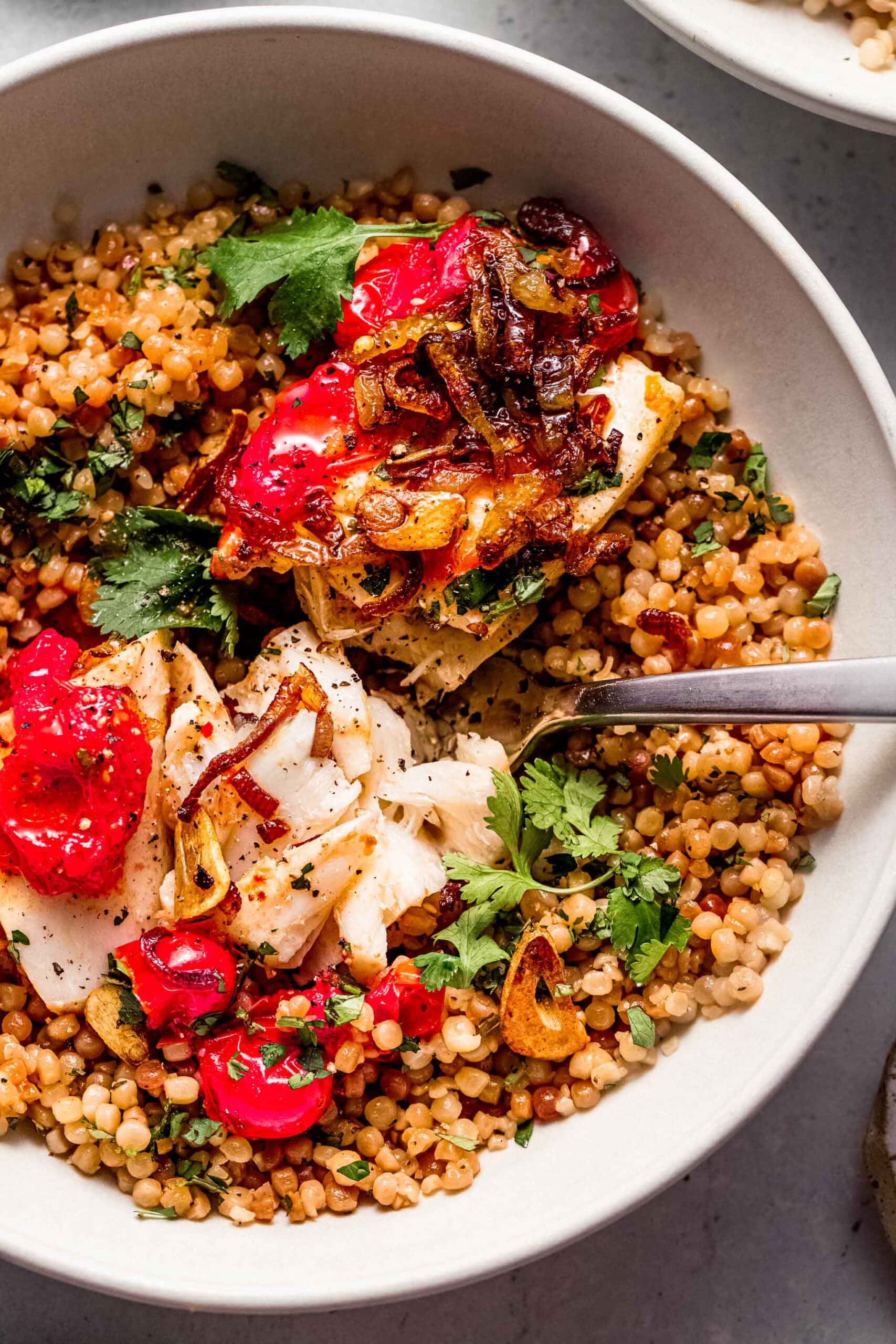 Poached fish topped with crispy shallots served over bowl of couscous.