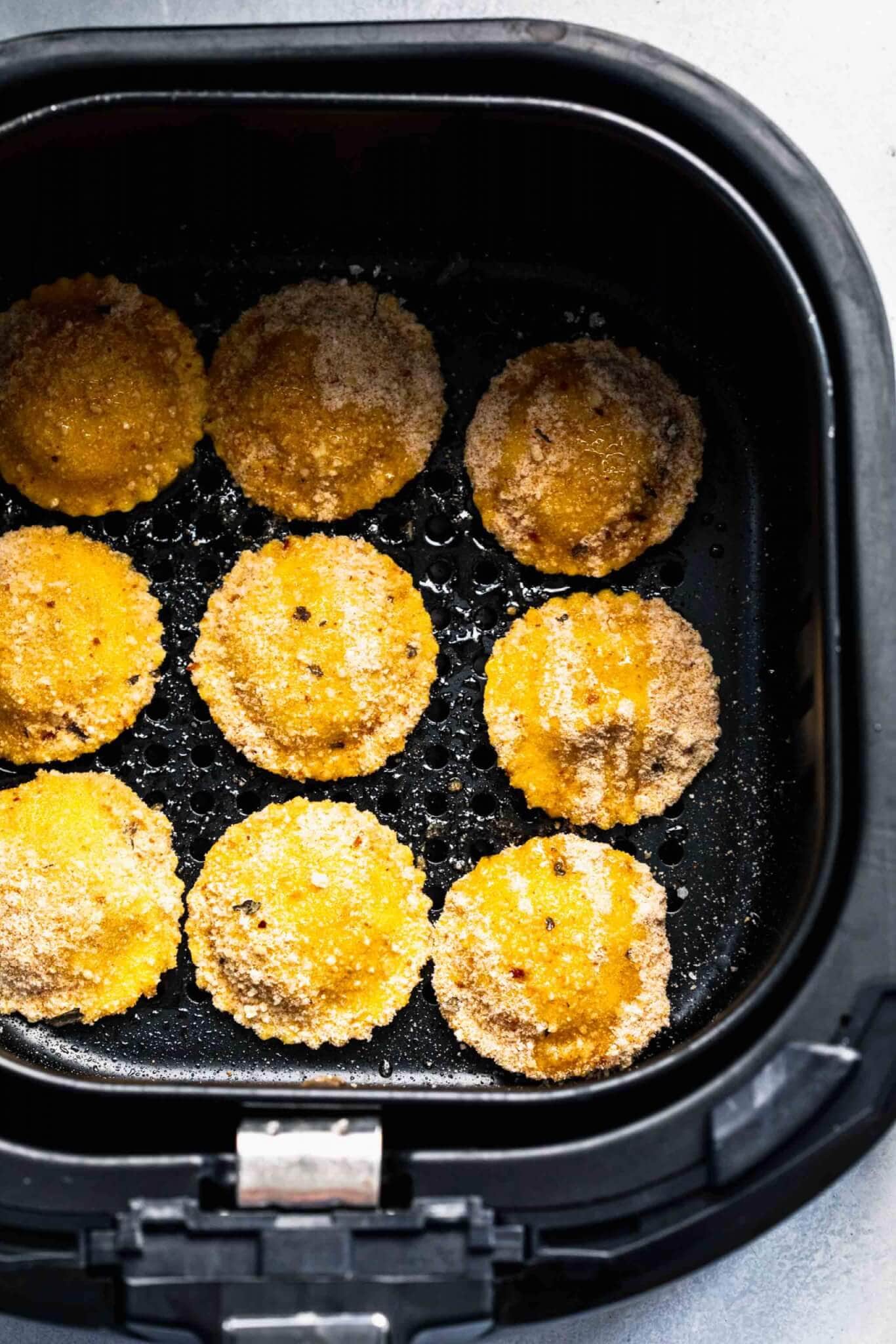 Breaded ravioli in air fryer basket.