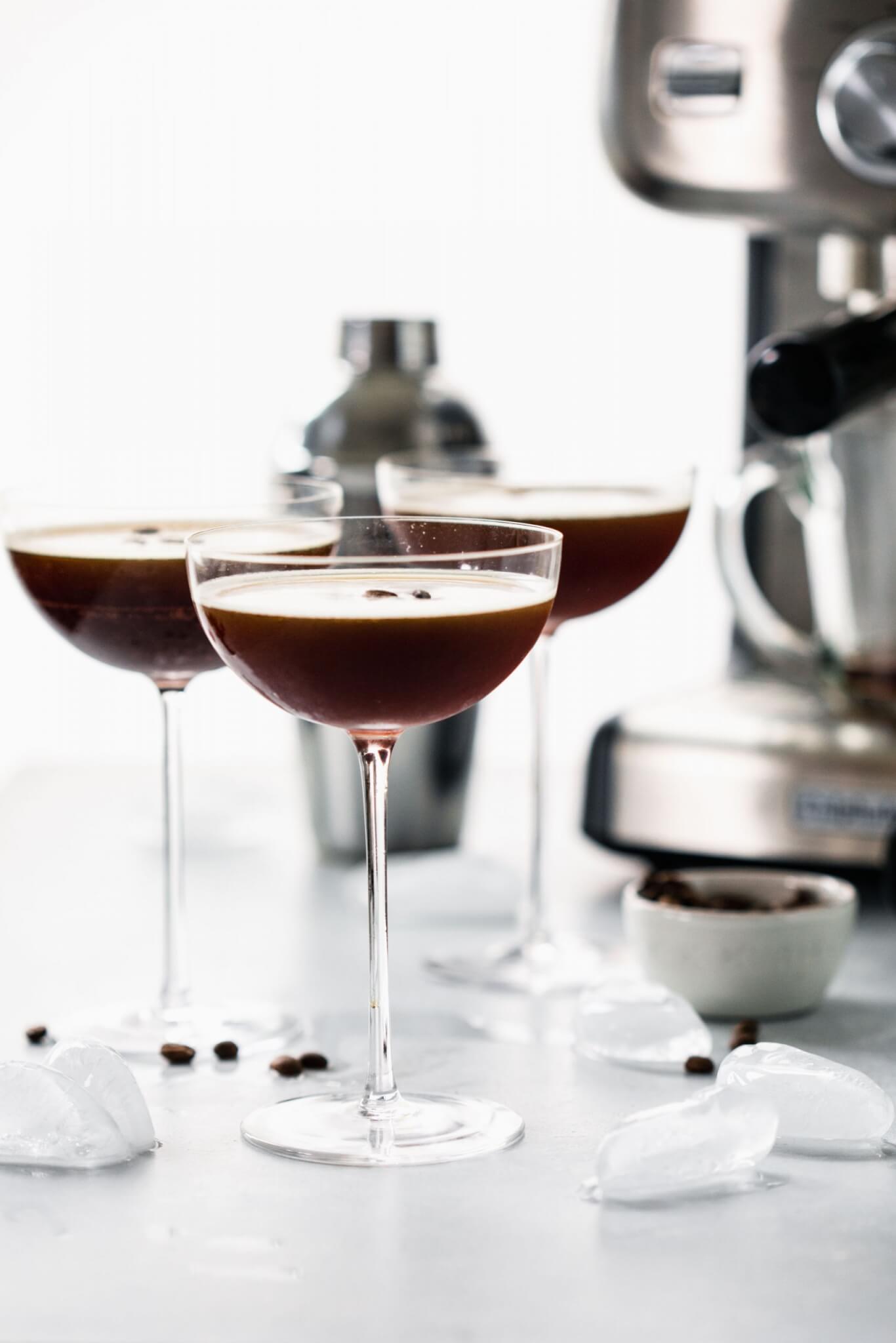 Three glasses of espresso martini on counter next to small bowl of coffee beans.