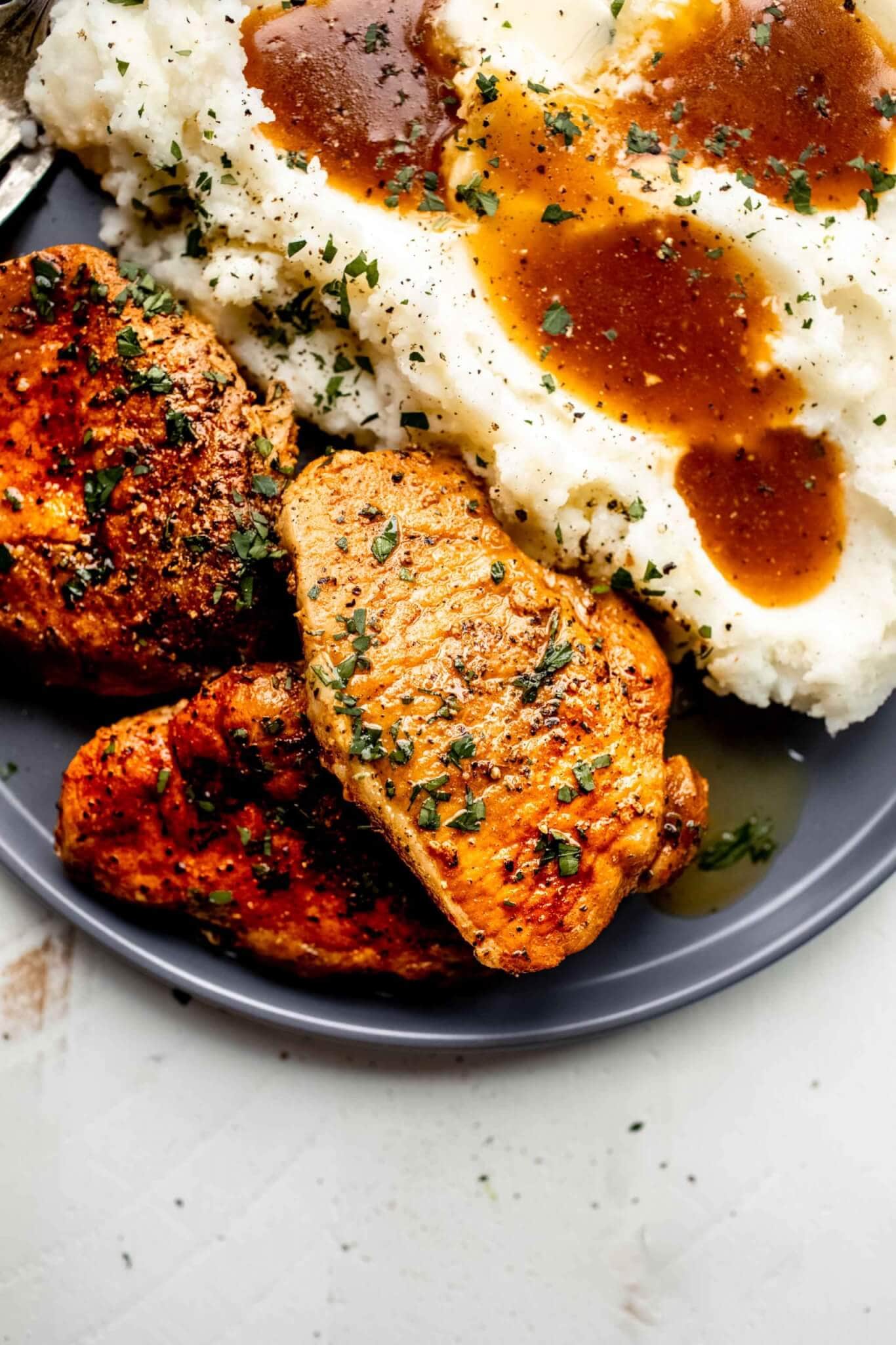 Three pork chops arranged on grey plate with mashed potatoes and gravy.