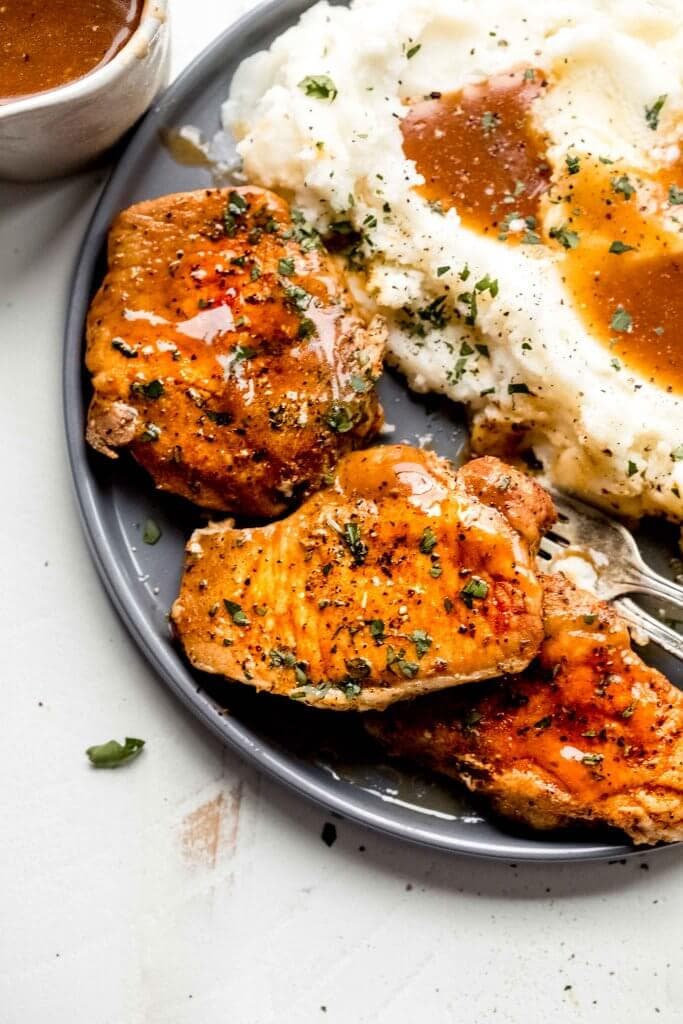 Three pork chops arranged on grey plate with mashed potatoes and gravy.