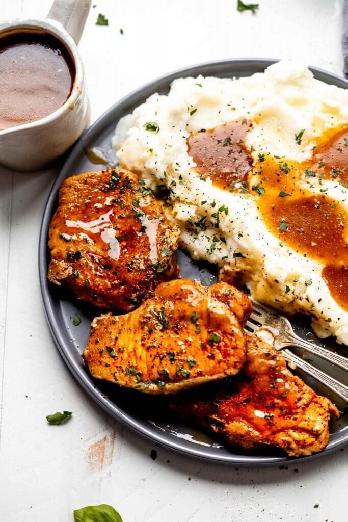 Three pork chops arranged on grey plate with mashed potatoes and gravy.