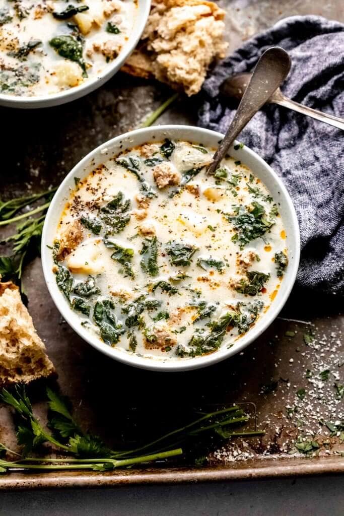 Two bowls of zuppa toscana on serving tray next to pieces of crusty bread.