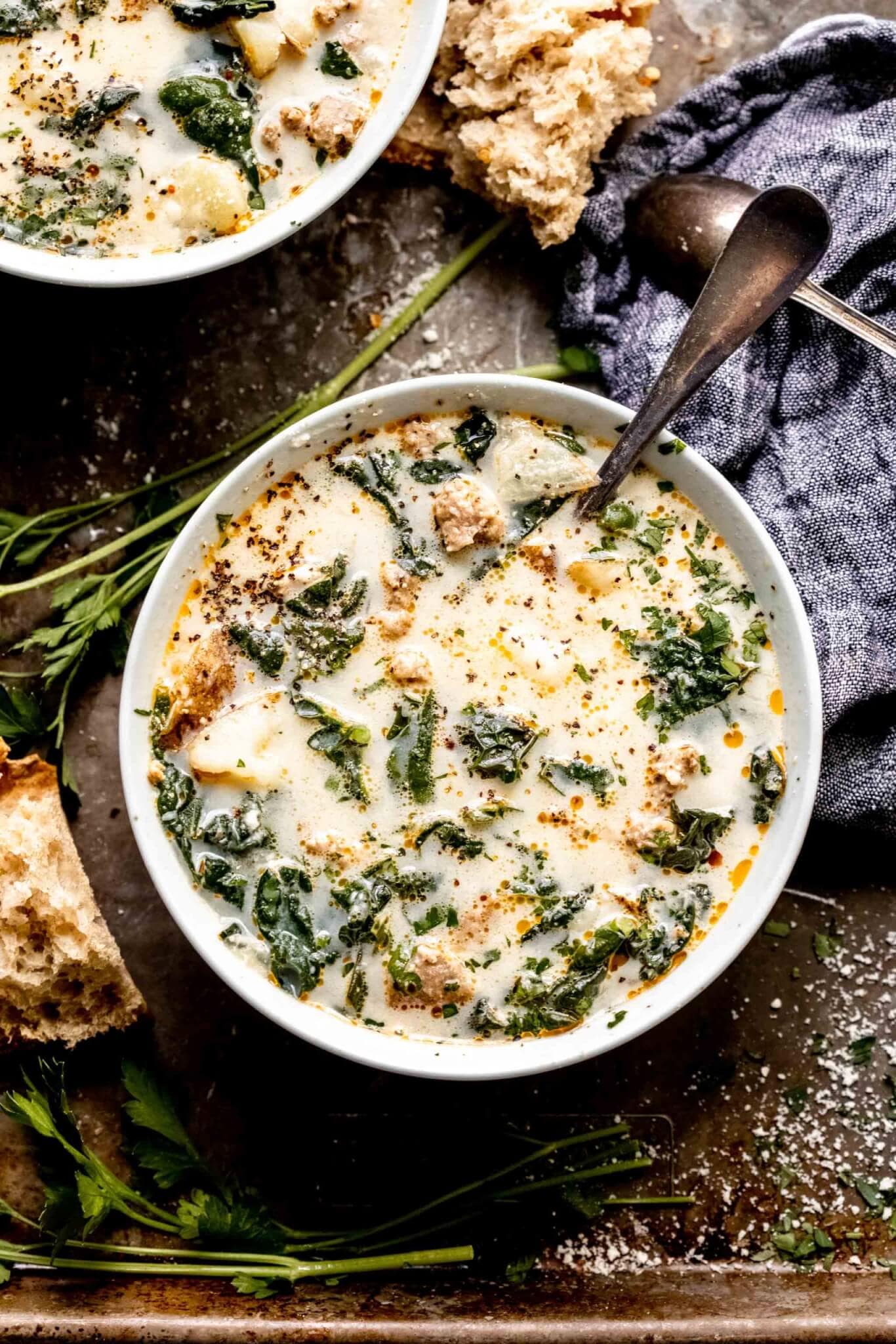 Two bowls of zuppa toscana on serving tray next to pieces of crusty bread.
