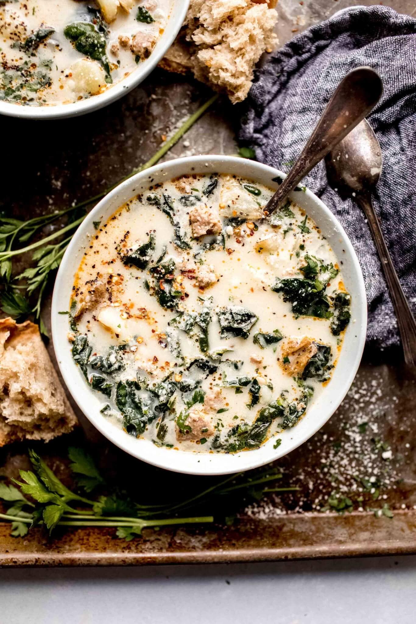 Two bowls of zuppa toscana on serving tray next to pieces of crusty bread.