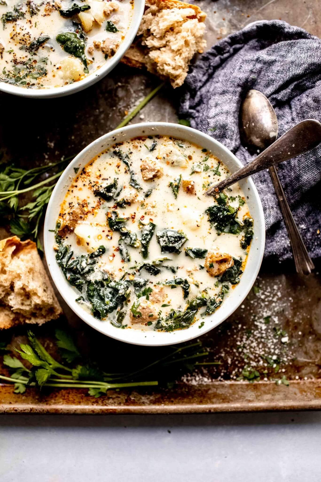 Two bowls of zuppa toscana on serving tray next to pieces of crusty bread.