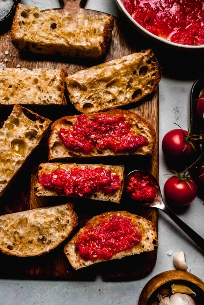 Pan con tomate on board next to tomatoes and flaky salt container.