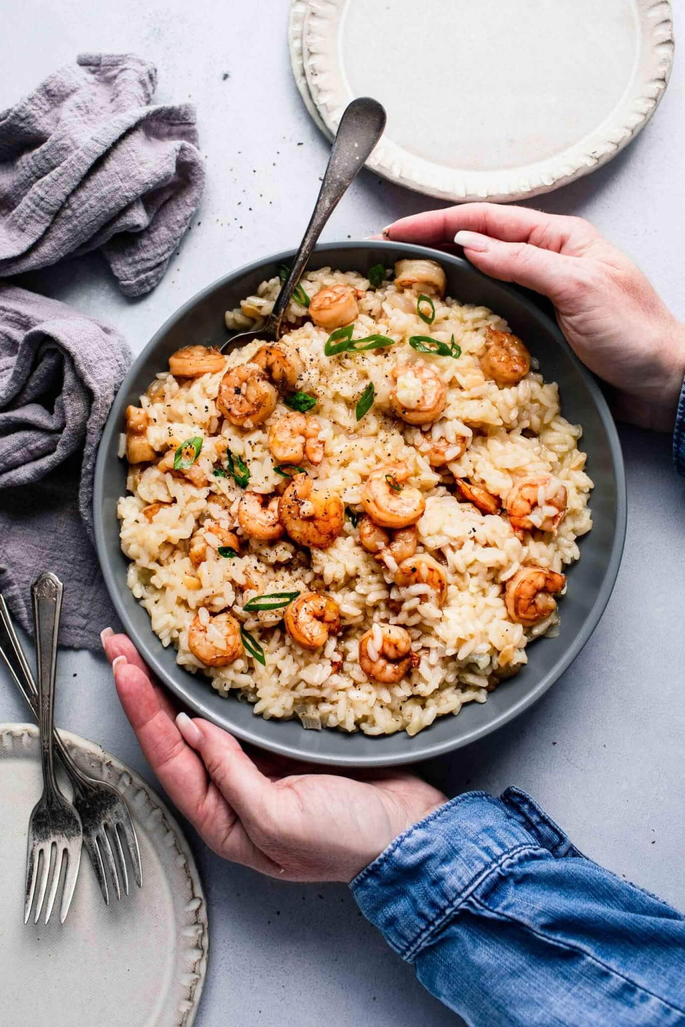 Hands holding bowl of prepared shrimp risotto.