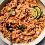 Shredded salsa chicken in bowl with lime wedges.