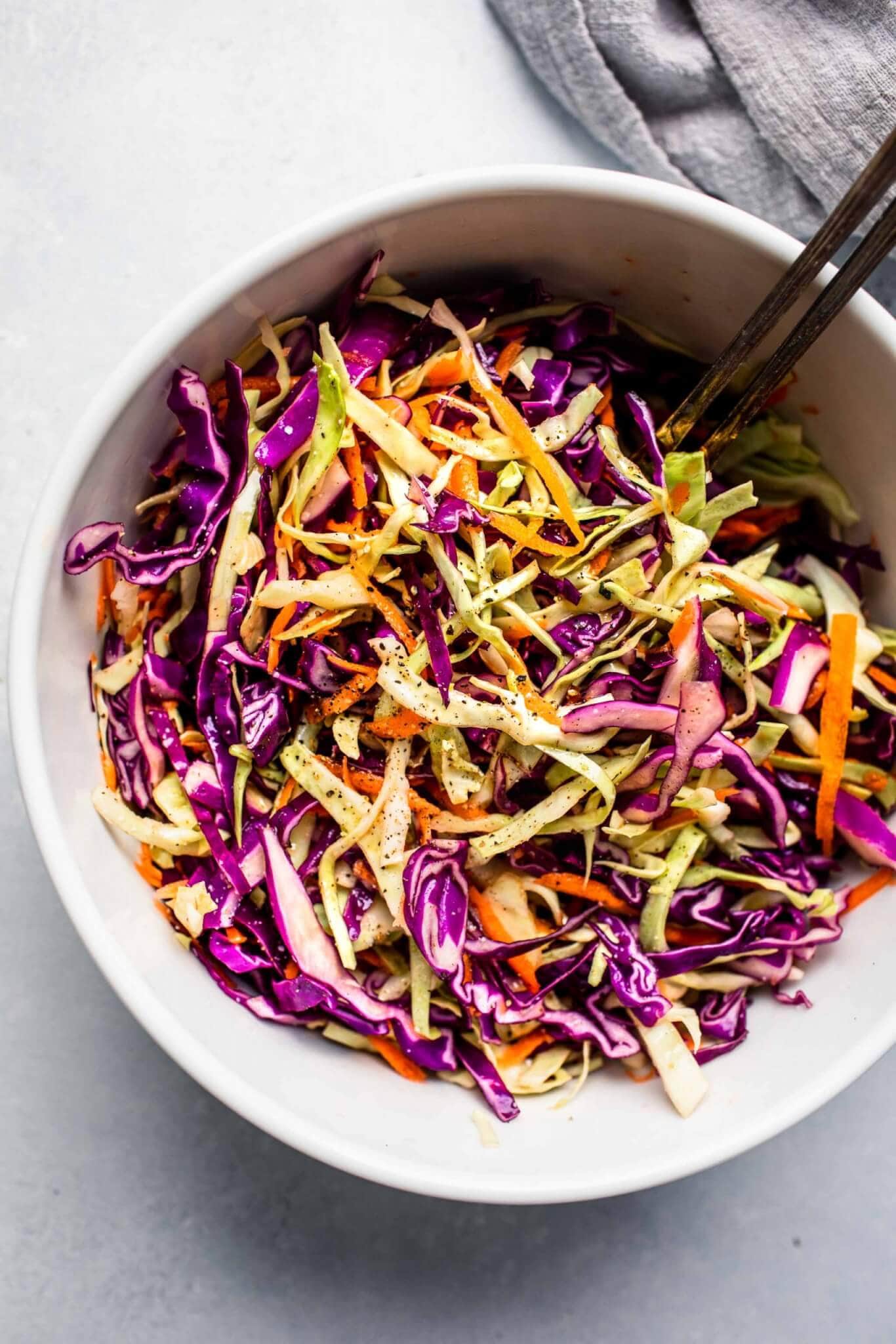 Vinegar slaw in large mixing bowl with serving utensils.