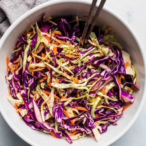 Vinegar slaw in large mixing bowl with serving utensils.
