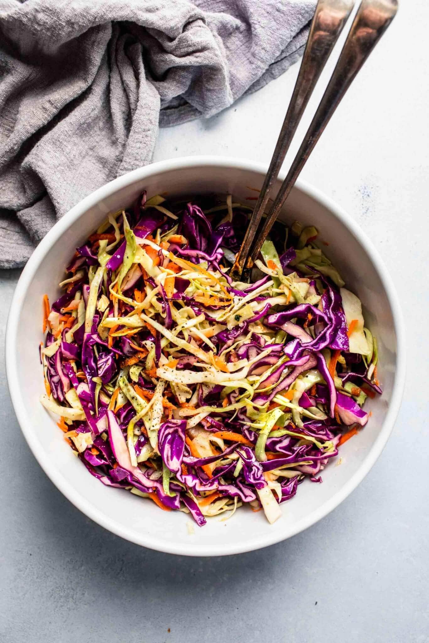 Overhead shot of vinegar slaw in large mixing bowl with serving utensils.