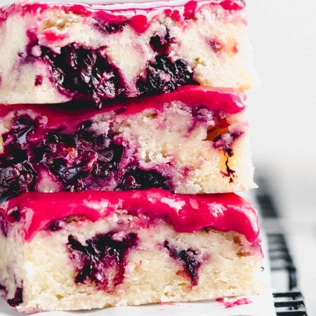 Extreme close up of three blackberry lemon blondies stacked on top of eachother next to bowl of blackberries.