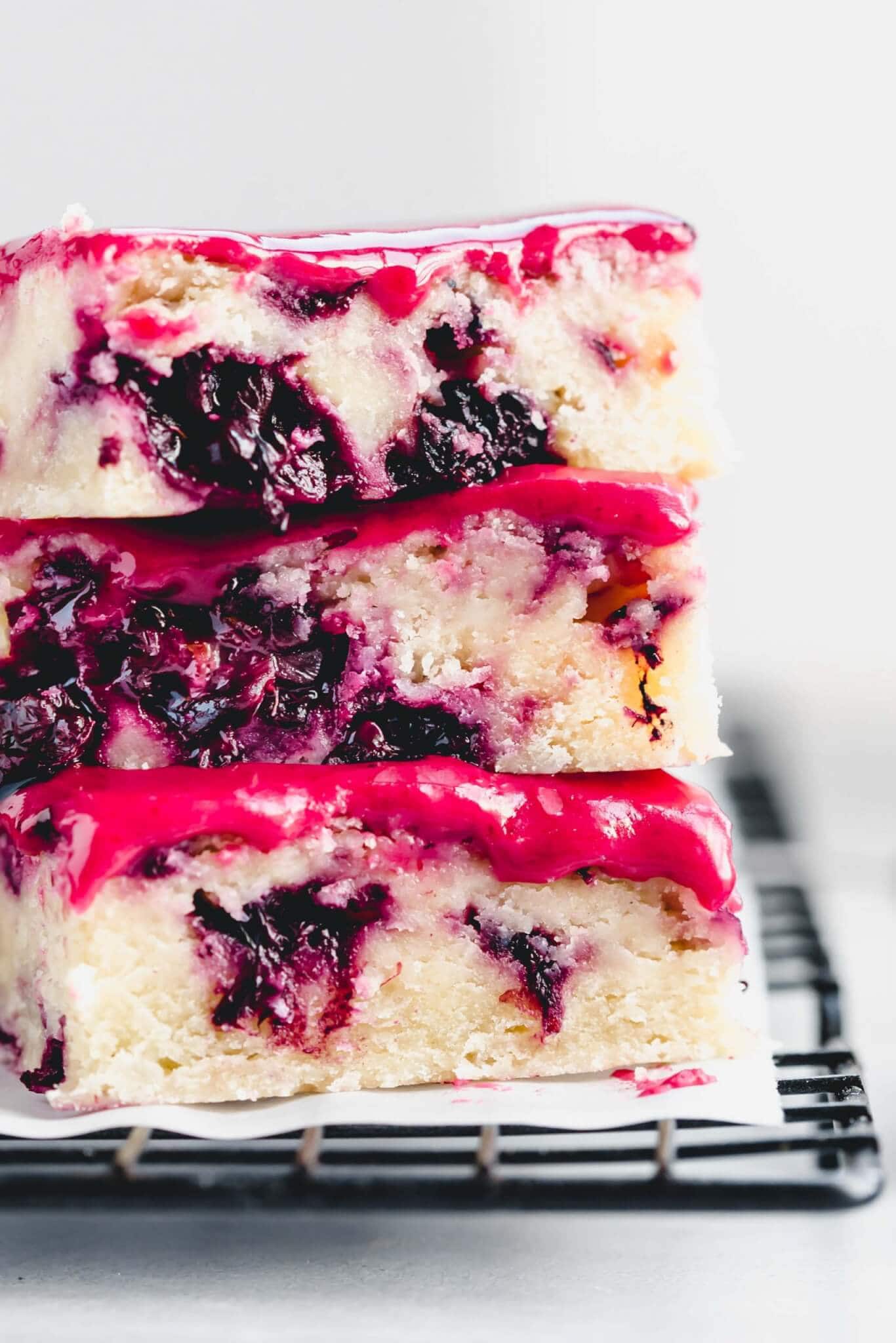 Extreme close up of three blackberry lemon blondies stacked on top of eachother next to bowl of blackberries.