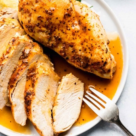 Two cooked chicken breasts out of instant pot on white plate, one sliced into pieces.
