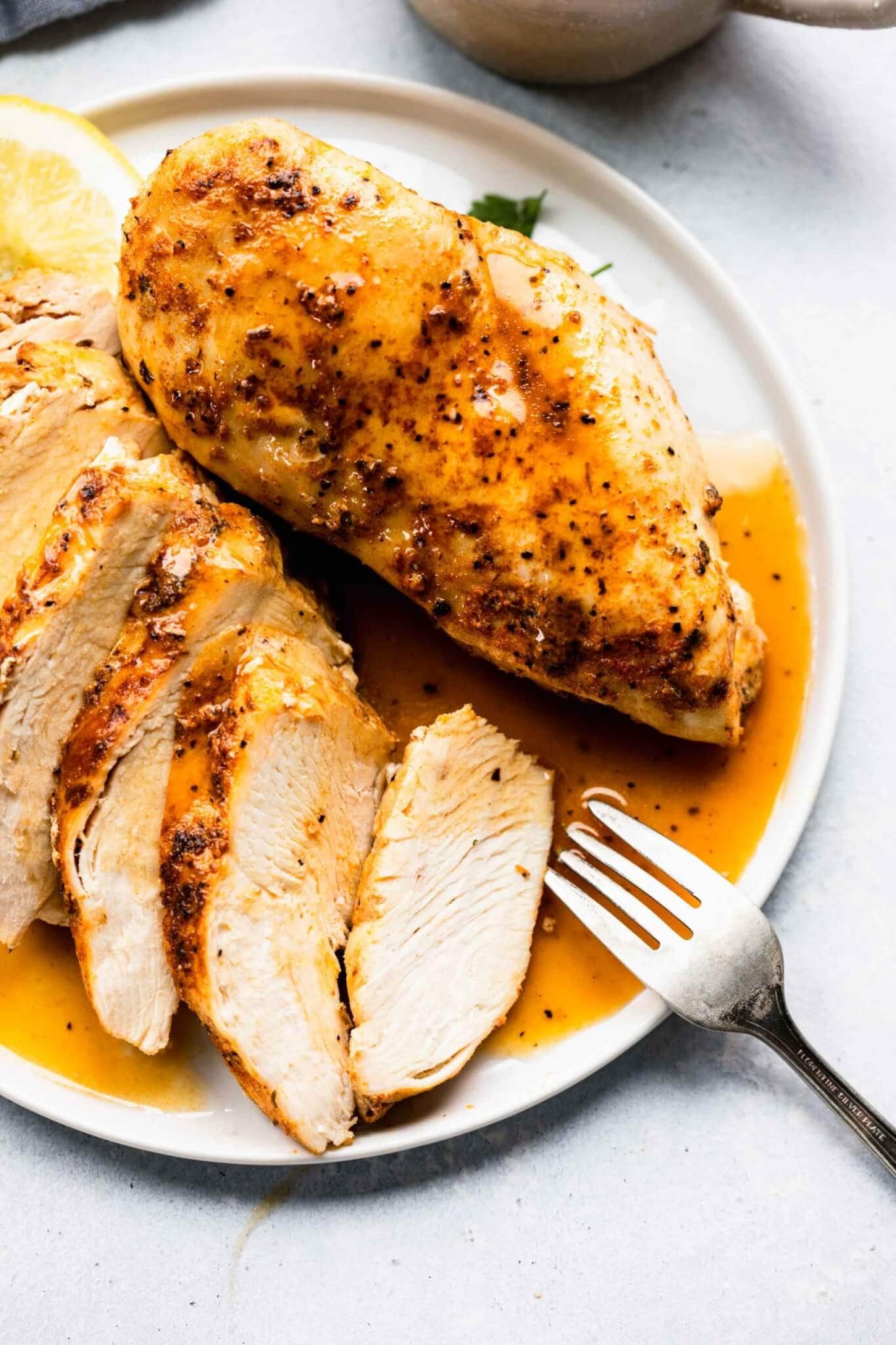 Two cooked chicken breasts out of instant pot on white plate, one sliced into pieces.