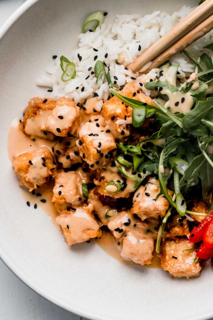 Spicy peanut tofu arranged on bowl of rice with black sesame seeds. 