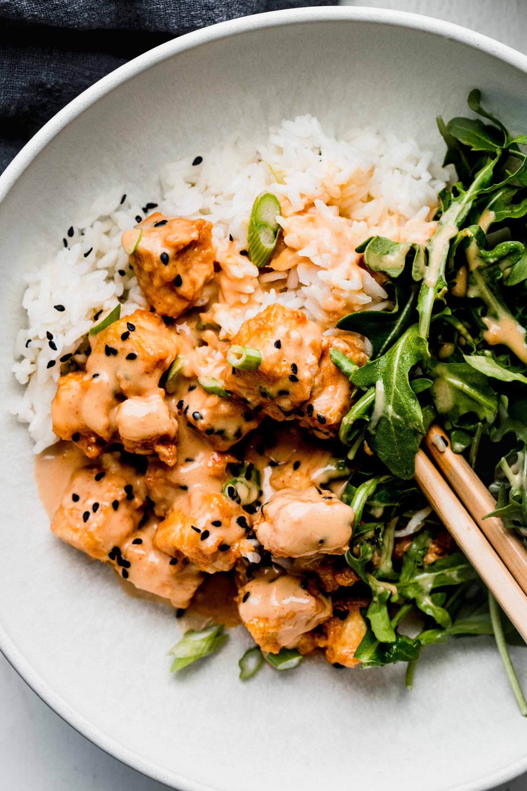 Spicy peanut tofu on bowl of rice with arugula.