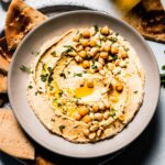 Hummus in bowl topped with macadamia nuts and parsley.