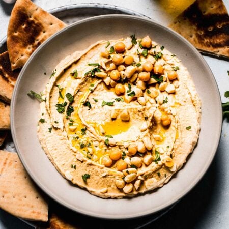 Hummus in bowl topped with macadamia nuts and parsley.