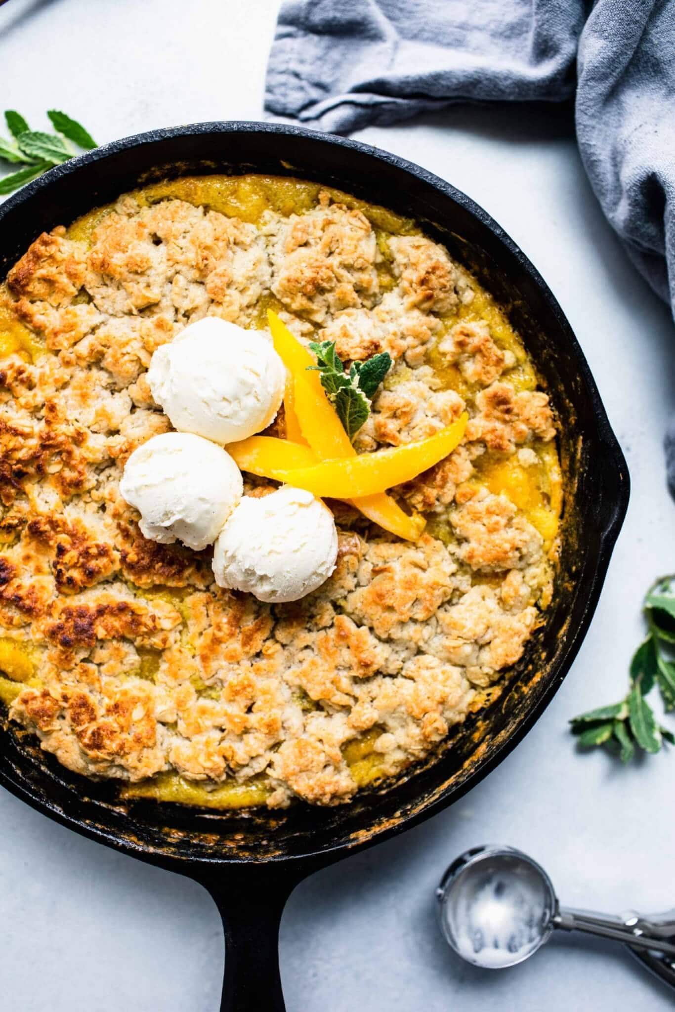 Cooked mango cobbler in skillet topped with ice cream.