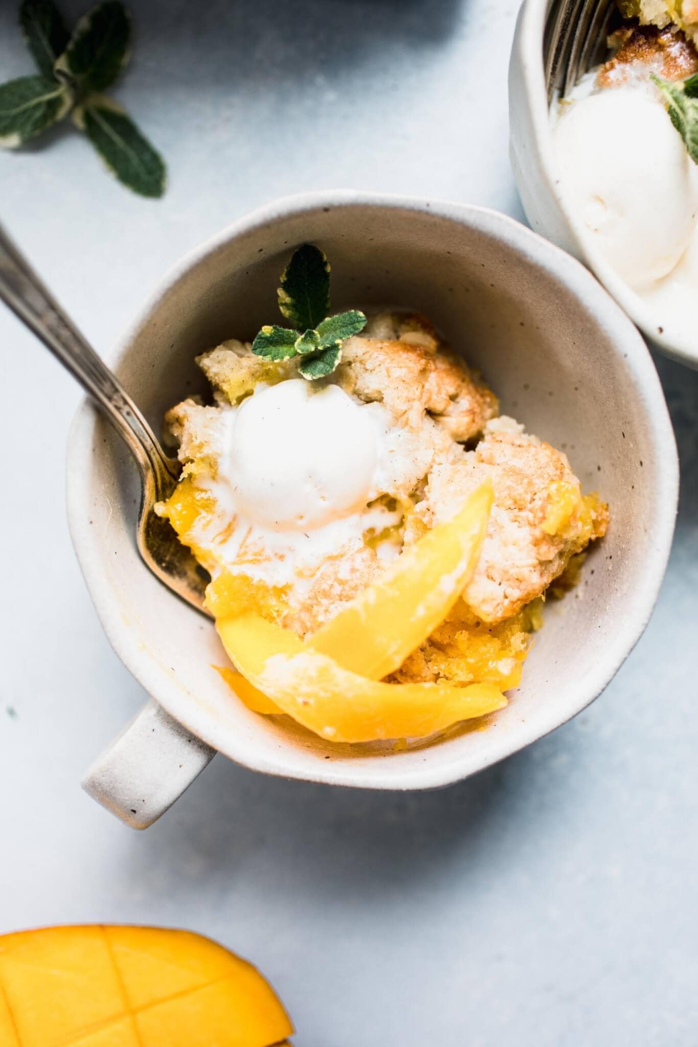 Mango cobbler in a mug topped with ice cream and mint sprig.