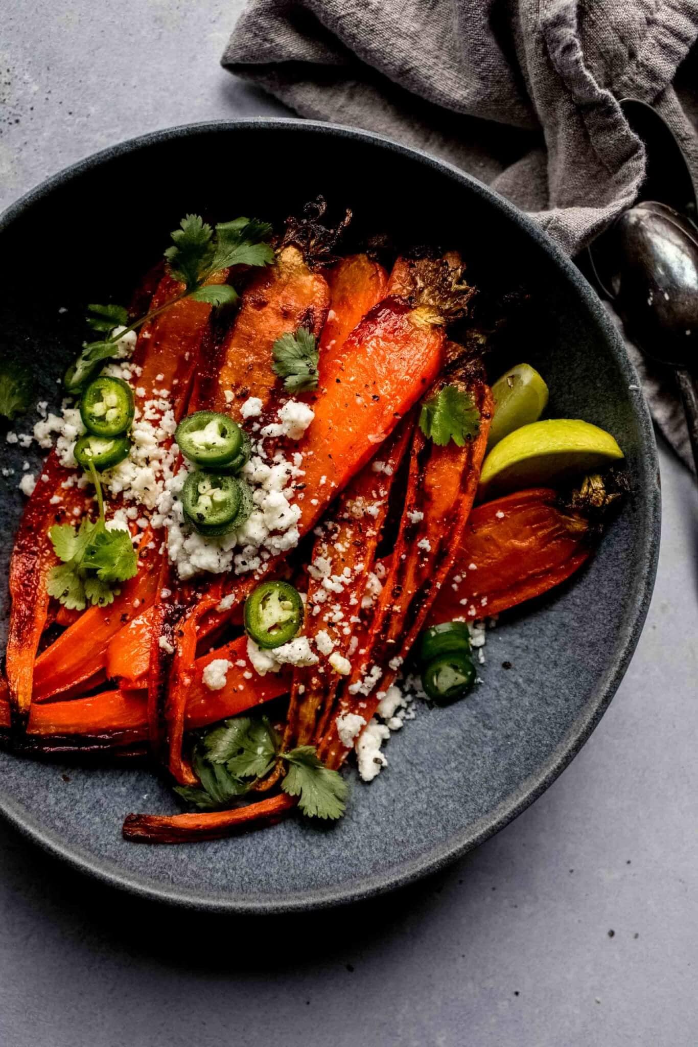 Roasted carrots in grey bowl topped with jalapenos and cotija cheese.