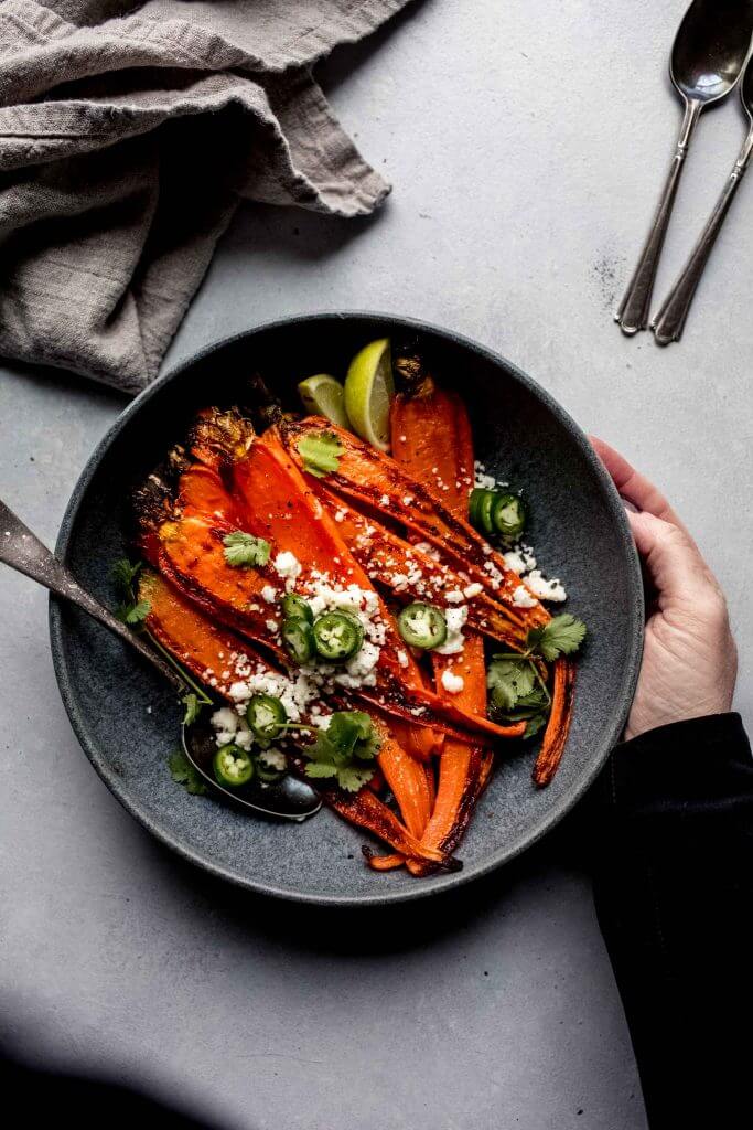 Hand holding bowl of oven roasted carrots. 